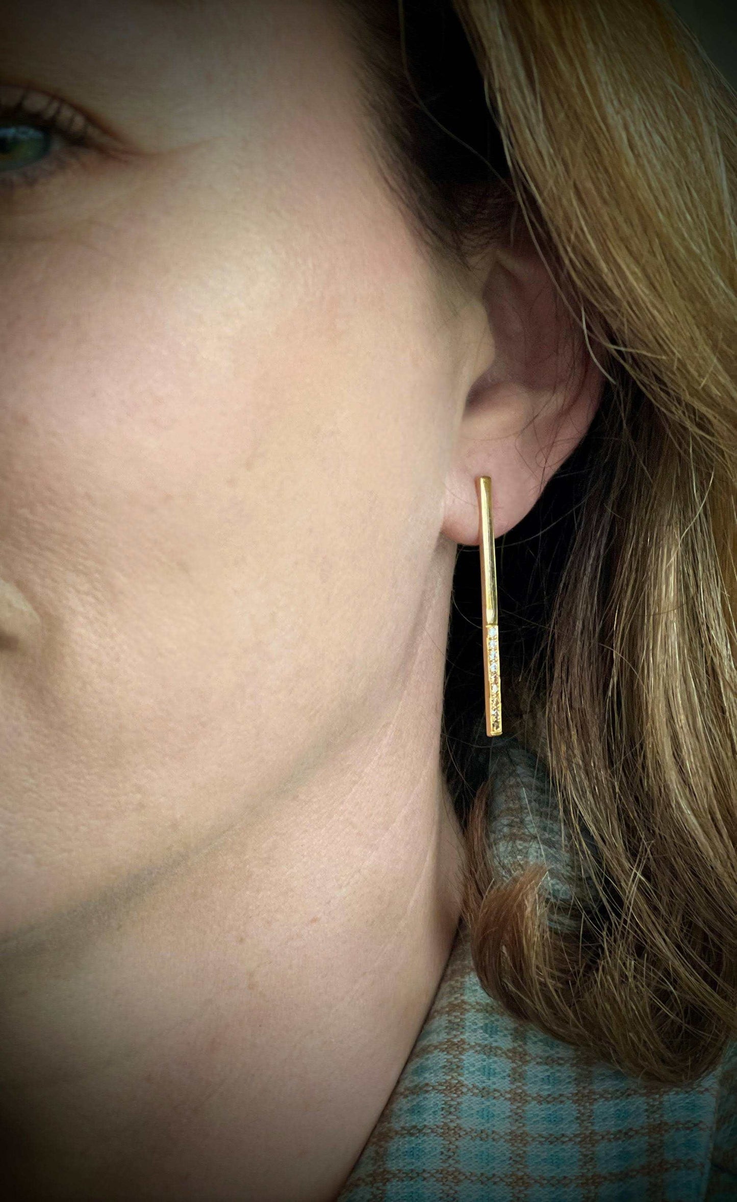 Dawn oorbel van Olivia Peeters Master Goldsmith, close-up van een gouden oorbel met een slank ontwerp, bezet met een rij fonkelende diamanten, gedragen door een vrouw met lichtbruin haar.