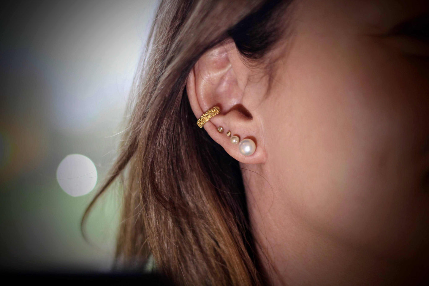 Doting dots ear cuff van olivia peeters master goldsmith: gouden ear cuff met een textuur van kleine bolletjes, gedragen aan het oor samen met een parel oorbel en kleine gouden studs.