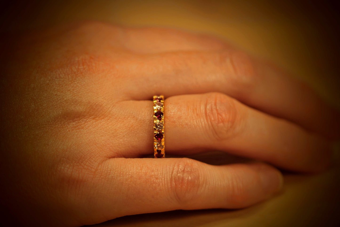 Eternal Embrace van Olivia Peeters Master Goldsmith: Gouden ring met een verfijnd ontwerp, bezet met afwisselende rode en witte edelstenen, gedragen aan een hand en gepresenteerd in warm licht.