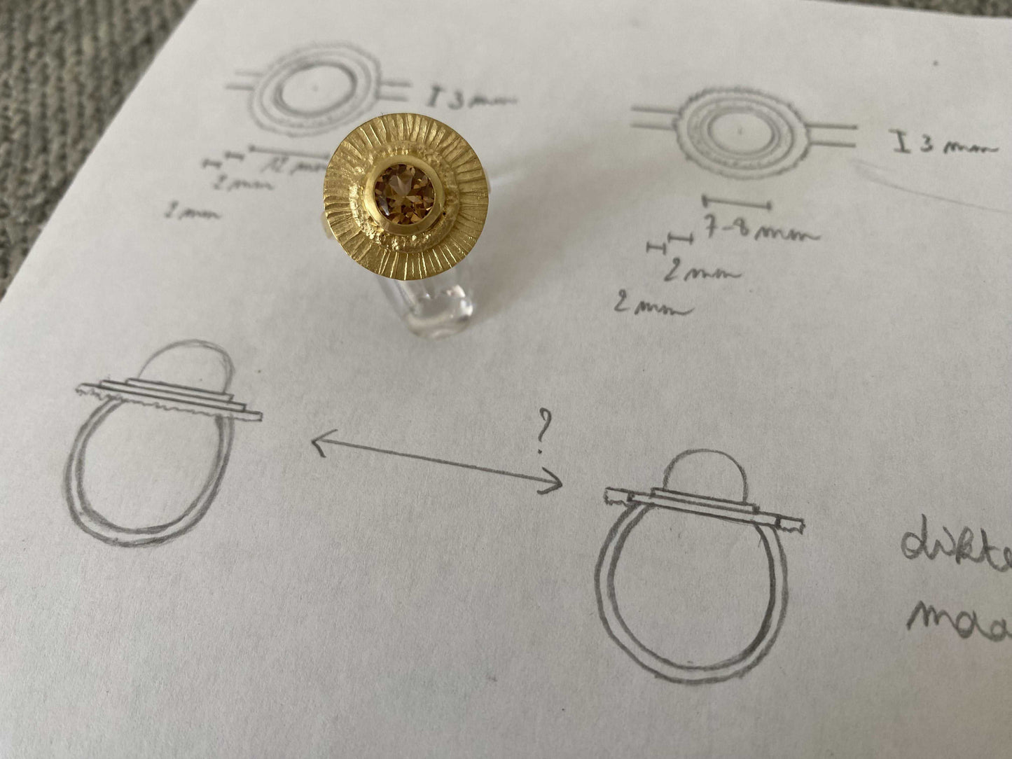 Ontwerpschets van de Fall Ring van Olivia Peeters Master Goldsmith: Een goudkleurige ring met een uitgesproken zonnestraalpatroon, naast technische schetsen die dimensies en details van het ontwerp illustreren. Perfecte weergave van het ontwerpproces en vakmanschap.