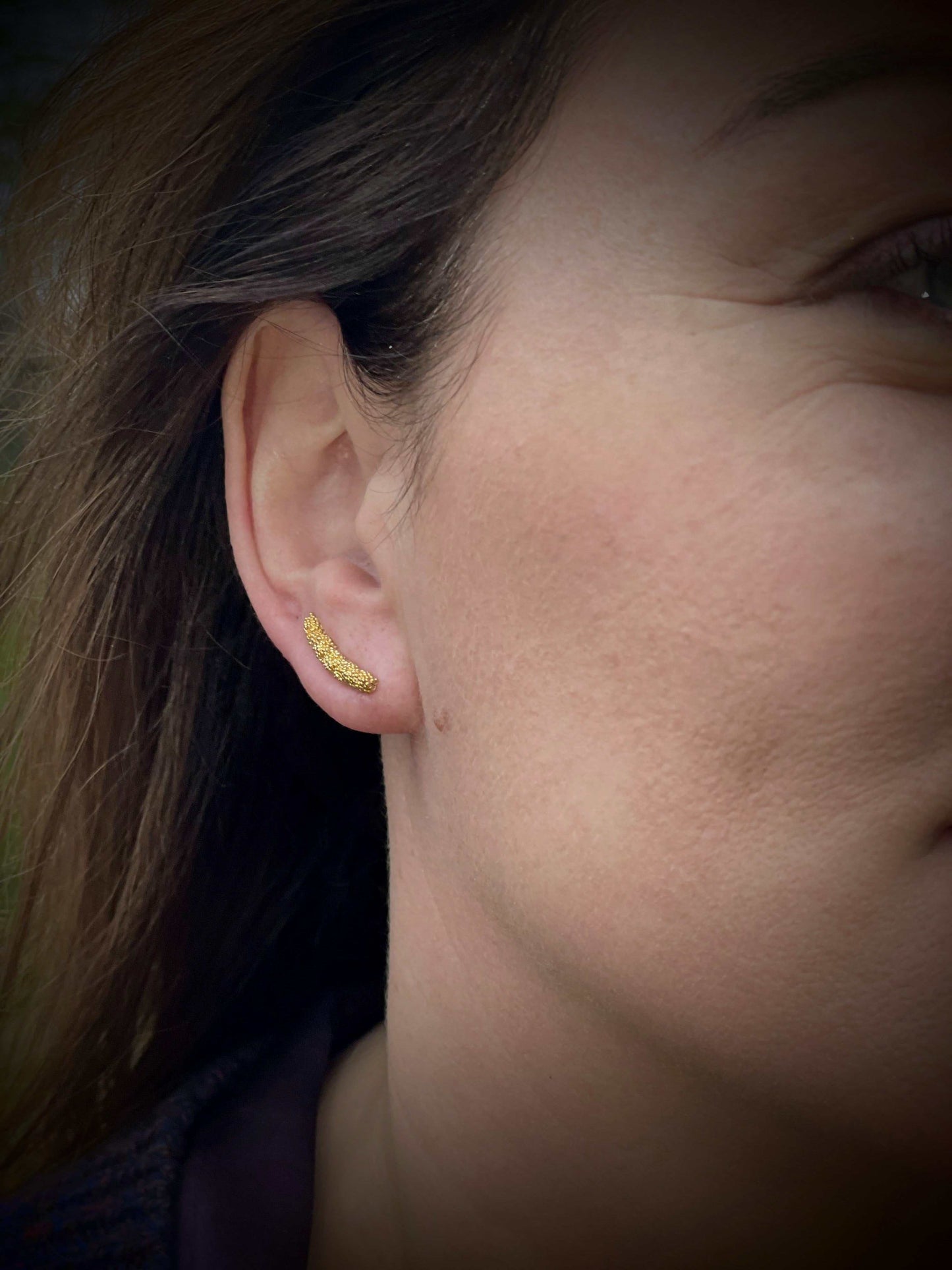 Pupa Ear Climbers-oorbellen van Olivia Peeters Master Goldsmith: Fijne gouden oorbellen met een subtiele bolletjesstructuur, gedragen aan het oor en gefotografeerd tegen een natuurlijke achtergrond voor een verfijnde uitstraling.