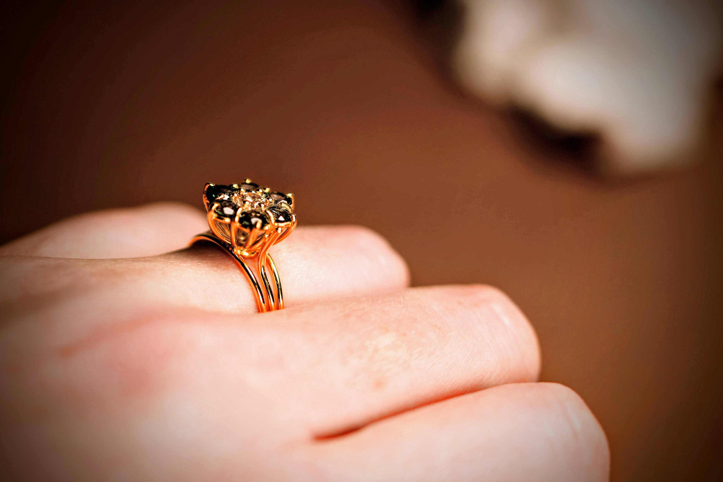 Green Blossom ring van Olivia Peeters Master Goldsmith, gedragen op een hand. De ring toont een bloemvormig ontwerp met een centrale lichtgroene steen, omringd door donkere groene stenen. De gouden zetting en het verfijnde bloemmotief komen tot leven tegen de warme tint van de huid en een zachte bruine achtergrond.