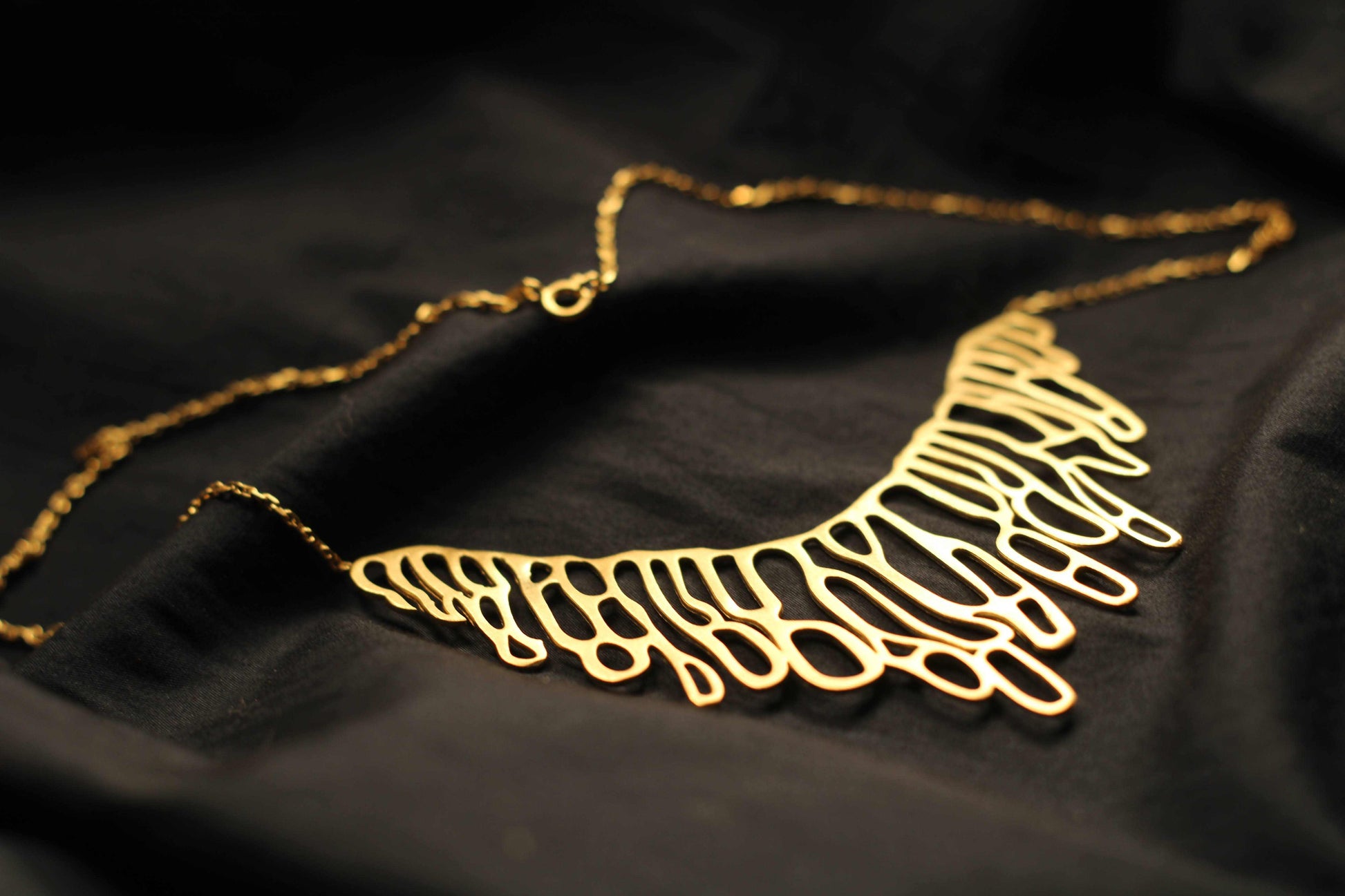Dewdrip necklace van Olivia Peeters Master Goldsmith: Gouden halsketting met organische, natuurlijke, abstracte, opengewerkte vormen, liggend op een zwarte achtergrond.