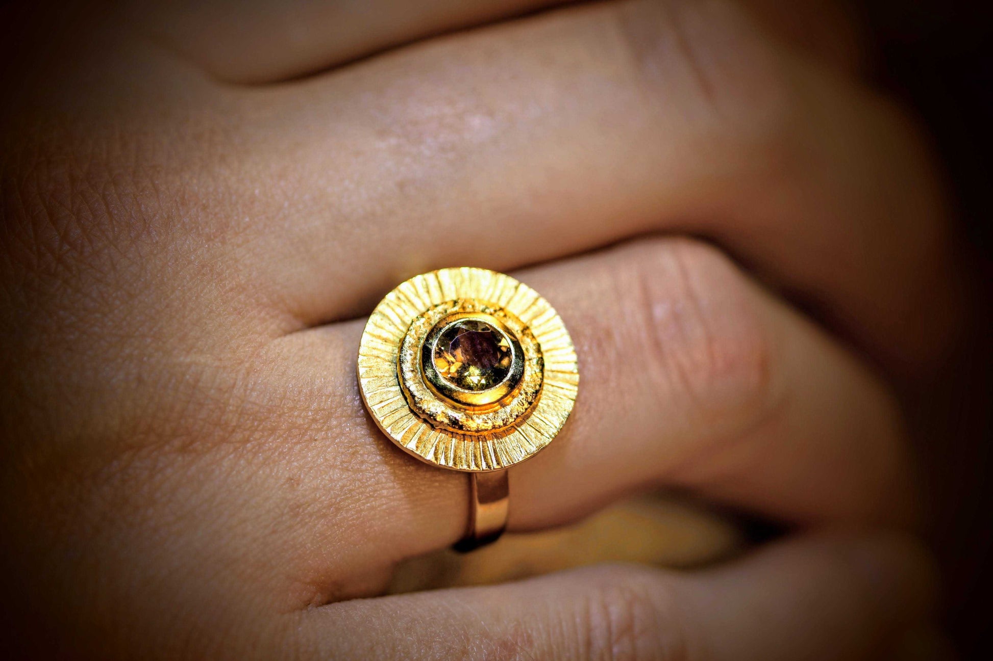 Fall Ring van Olivia Peeters Master Goldsmith: Gouden ring met een unieke structuur, een centraal geplaatste toermalijn omringd door zonnestraalpatronen, gedragen aan een hand en sfeervol vastgelegd in warm licht.