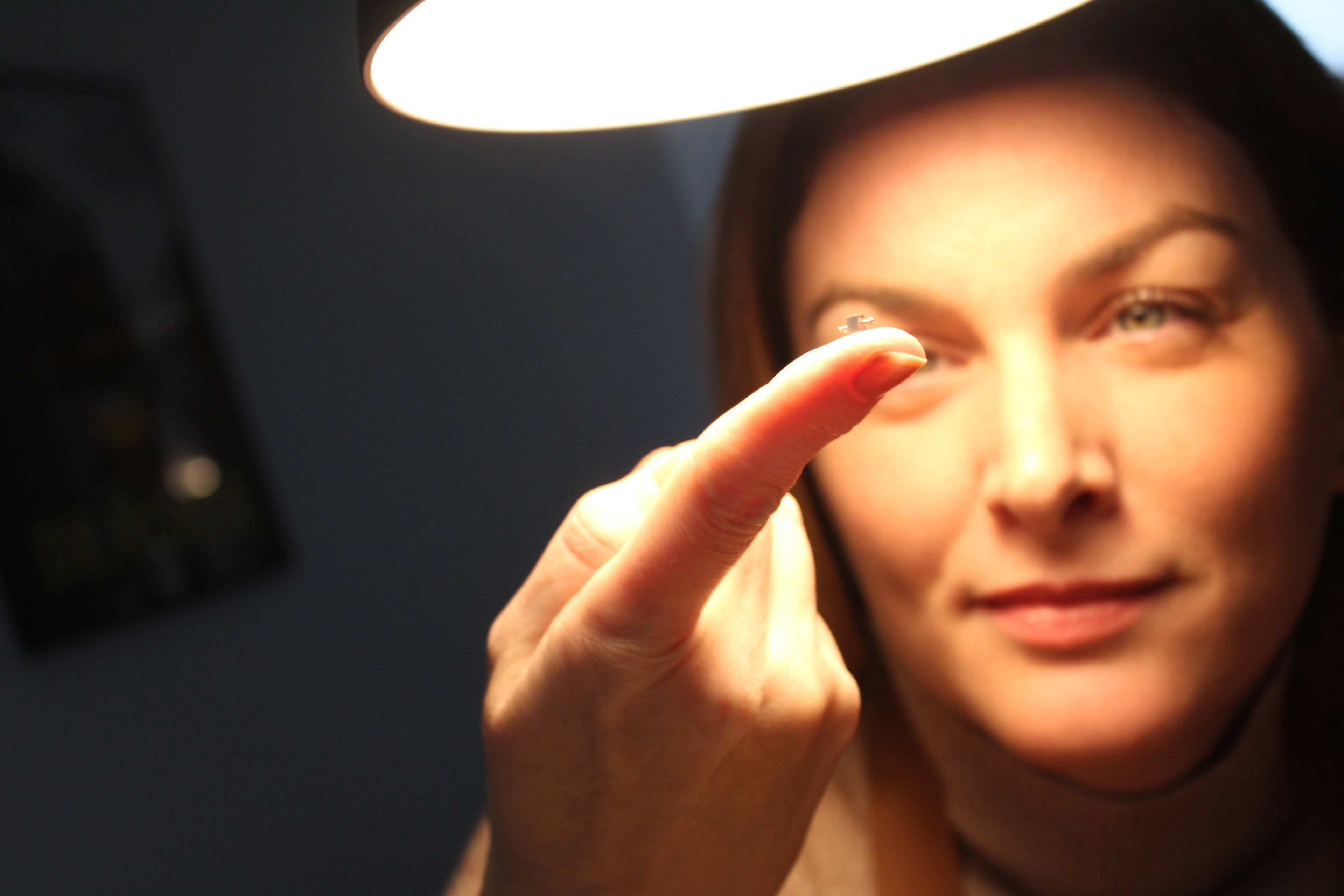 Een vrouw, zacht verlicht door een lamp, richt haar aandacht op een kleine edelsteen die ze voorzichtig op het puntje van haar vinger balanceert, symboliserend vakmanschap en precisie.