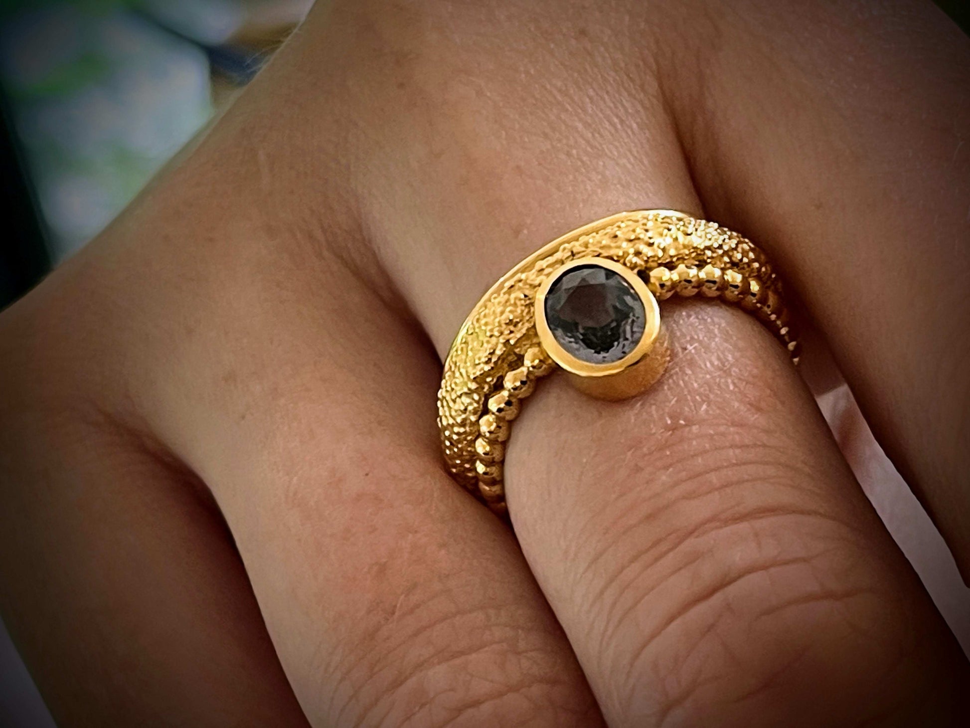 Stellwagen Ring van Olivia Peeters Master Goldsmith, een unieke gouden ring met een opvallend kralenontwerp en een donkere ovale edelsteen in een gladde zetting, gedragen aan een hand, met een subtiele achtergrond.