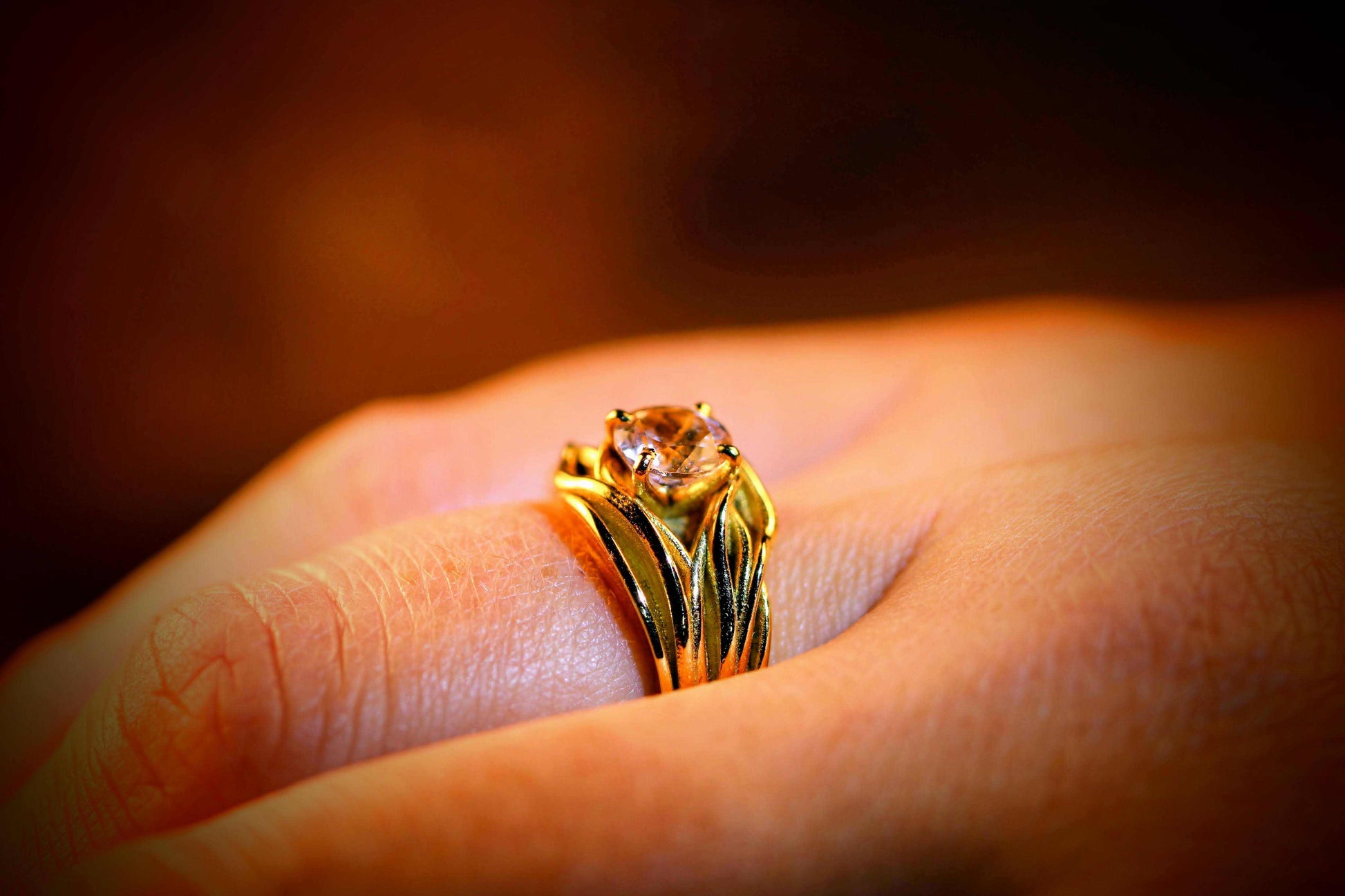 Sudden Wave Ring van Olivia Peeters Master Goldsmith, gedragen aan een vinger. De gouden ring heeft golvende lijnen die samenkomen bij een sprankelende steen in een stijlvolle zetting. Het ontwerp straalt elegantie en dynamiek uit, perfect vastgelegd in een warme, sfeervolle belichting.