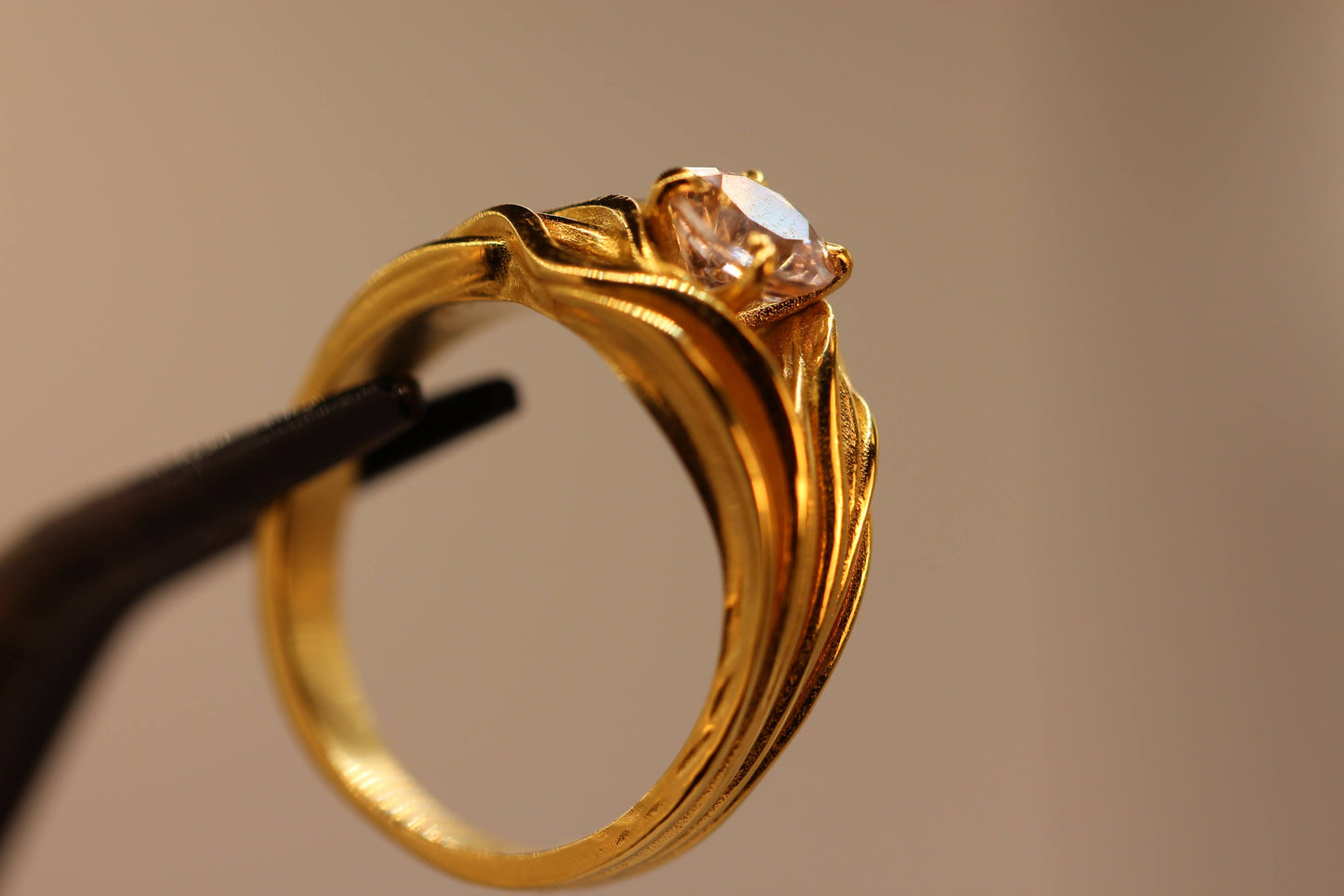 Sudden Wave Ring van Olivia Peeters Master Goldsmith, close-up gefotografeerd op een standaard. De gouden ring toont vloeiende, golvende lijnen die elegant naar een sprankelende centrale steen leiden. Het verfijnde ontwerp wordt belicht tegen een neutrale achtergrond, met de nadruk op de dynamische vormgeving en het vakmanschap.