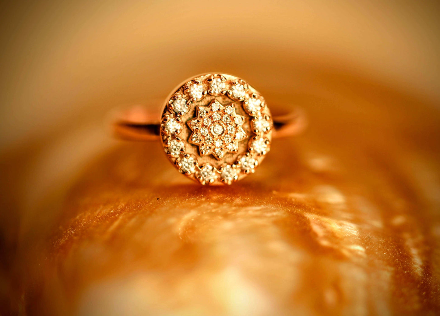 Gatsby van Olivia Peeters Master Goldsmith: Elegante gouden ring met een rond design in Art Deco-stijl, bezet met een symmetrisch patroon van fonkelende diamanten, gepresenteerd tegen een warme, gouden achtergrond.