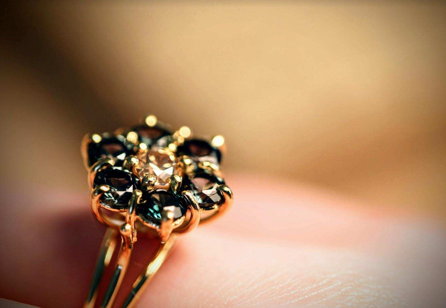 Green Blossom ring van Olivia Peeters Master Goldsmith, close-up gefotografeerd. De ring heeft een bloemvormig ontwerp met een centrale lichtgroene steen, omlijst door diepere groene stenen, allemaal in een delicate gouden zetting. Het ontwerp straalt natuurlijke elegantie en ambachtelijke precisie uit, met een subtiele achtergrond die de details van de ring benadrukt.