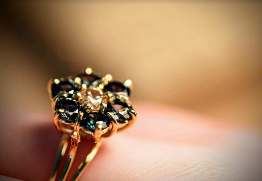 Green Blossom ring van Olivia Peeters Master Goldsmith, close-up gefotografeerd. De ring heeft een bloemvormig ontwerp met een centrale lichtgroene steen, omlijst door diepere groene stenen, allemaal in een delicate gouden zetting. Het ontwerp straalt natuurlijke elegantie en ambachtelijke precisie uit, met een subtiele achtergrond die de details van de ring benadrukt.