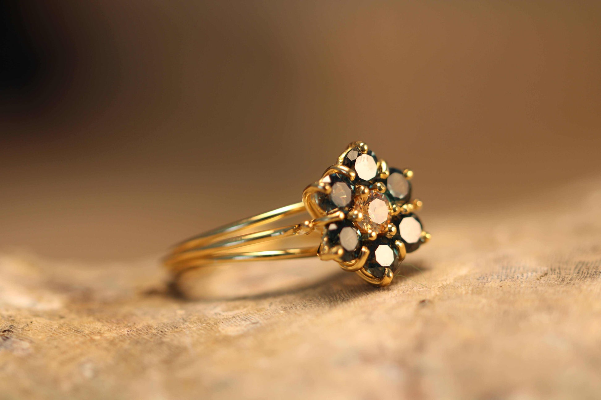 Green Blossom ring van Olivia Peeters Master Goldsmith, zijaanzicht. De ring heeft een bloemvormig ontwerp met een centrale lichtgroene steen, omringd door diepere groene stenen in een verfijnde gouden zetting. Het ontwerp wordt benadrukt tegen een zachte, neutrale achtergrond die de warme tinten van het goud en de schittering van de stenen versterkt.