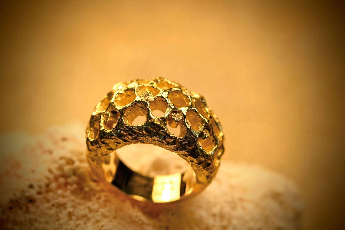 Honeycomb van Olivia Peeters Master Goldsmith: Gouden ring met een opvallend opengewerkt honingraatdesign, waarin delicate diamantjes schitteren, gepresenteerd op een zachte, beige ondergrond in warm licht.