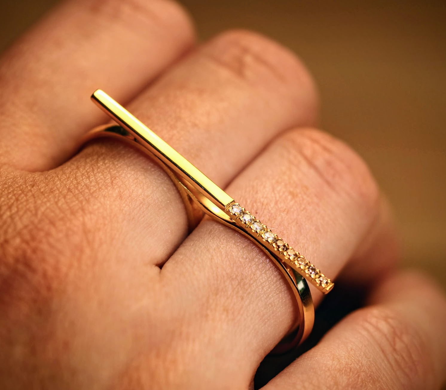 Morning Horizon van Olivia Peeters Master Goldsmith: Gouden ring met een strak modern ontwerp, voorzien van een rechte balk en een rij delicate diamanten, gedragen aan twee vingers en gepresenteerd in warm licht.