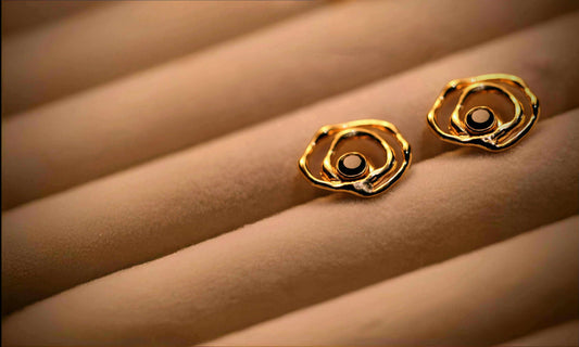 Ripple Drop studoorbellen van Olivia Peeters Master Goldsmith. Gouden oorringen met een organisch golvend ontwerp en een donkere edelsteen in het midden, gepresenteerd op een zachte sieradenhouder.